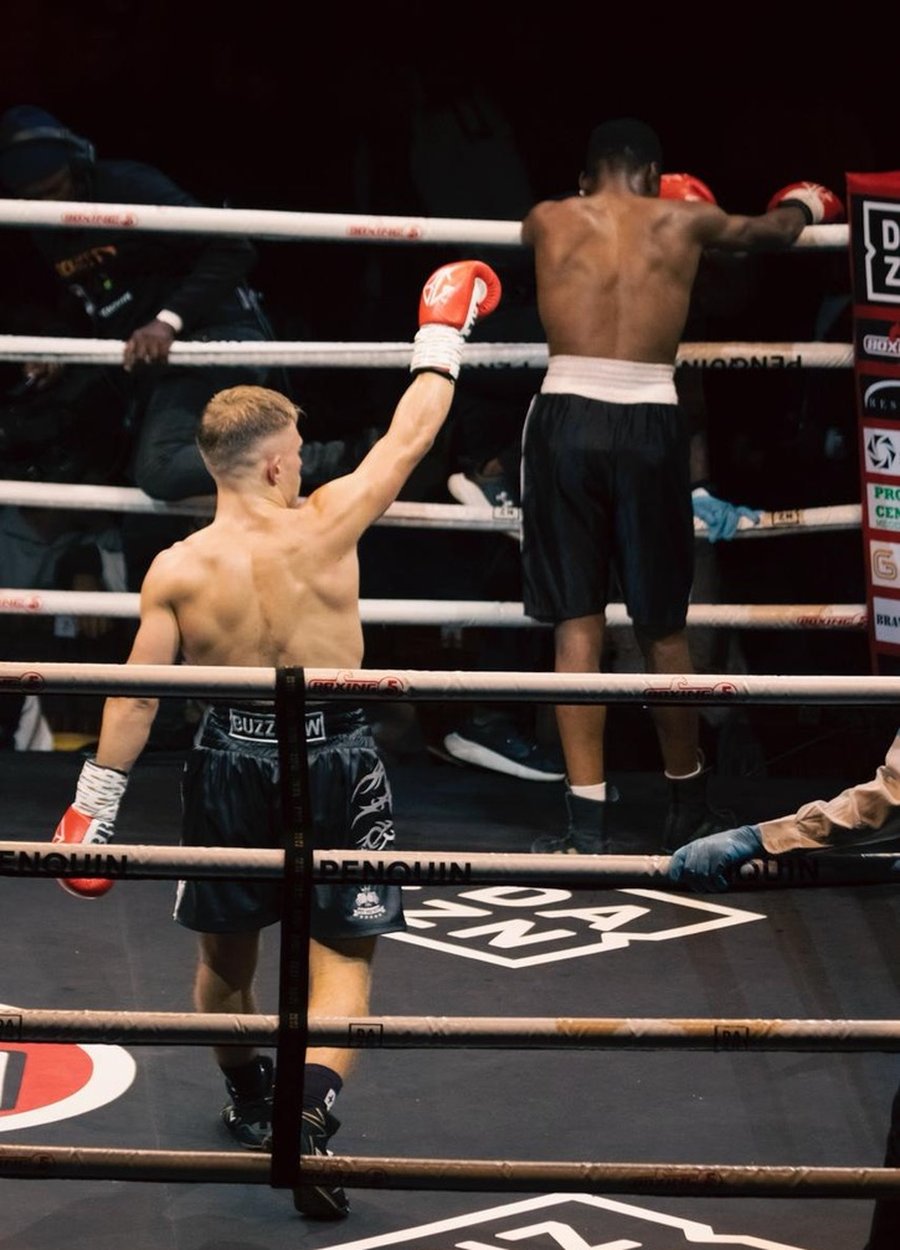 Doron with his back turned, raising a red glove in the ring after a fight.