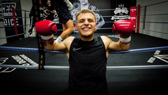 Doron smiling in a boxing ring with red gloves raised.