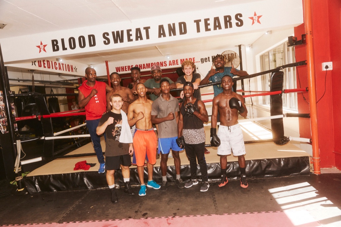 A youth boxing team poses together in front of a gym ring.