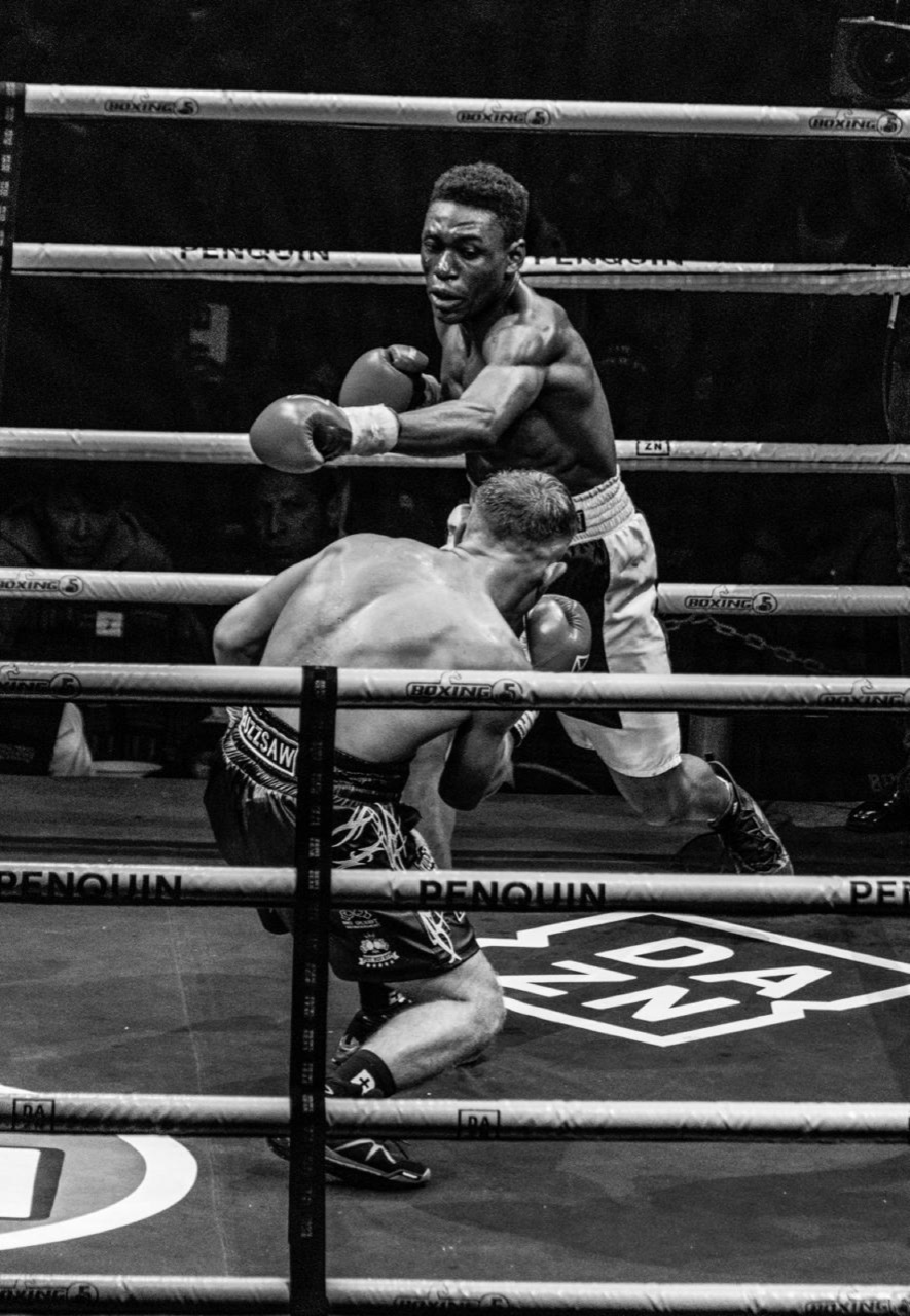 Black-and-white ringside view of a boxer throwing a punch.
