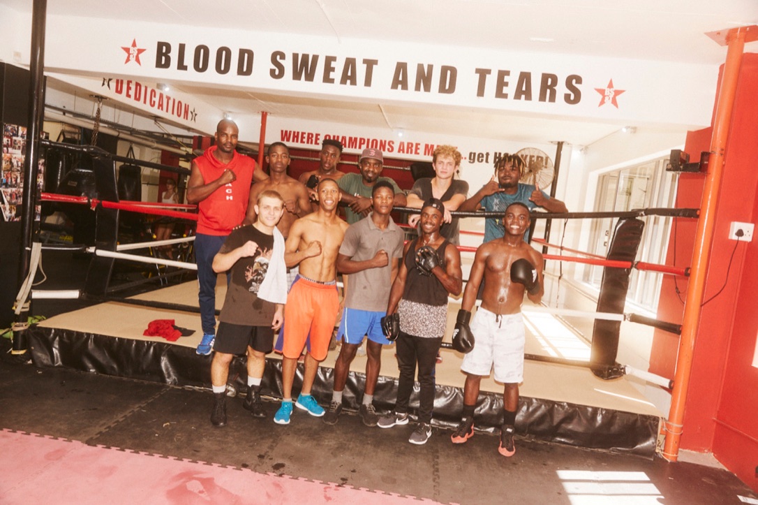 A youth boxing team poses together in front of a gym ring.