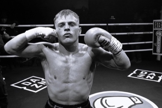 Black-and-white portrait of a boxer raising his gloves after a bout.