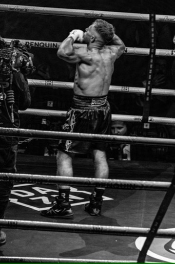 Black-and-white ringside portrait of a boxer raising both arms.