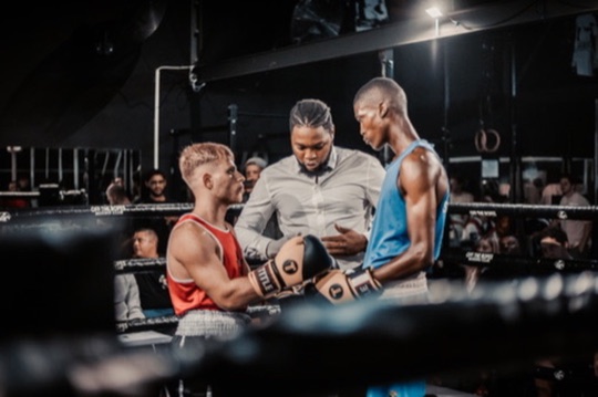 Two boxers and a referee stand together in the ring.