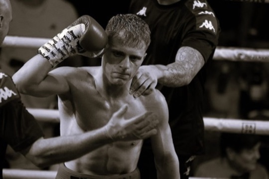 A boxer sits ringside while a coach works on his hand wraps.