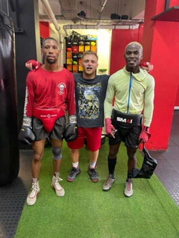 Three training partners stand together in a boxing gym.
