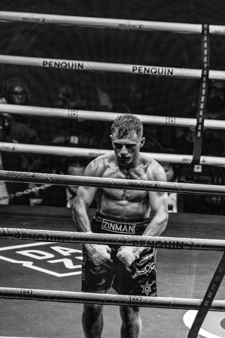 A boxer standing in the ring between the ropes, photographed in black and white.