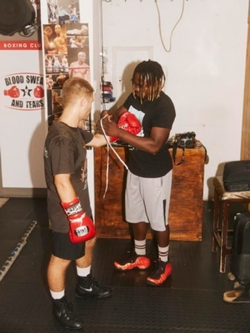 A coach fits a red boxing glove on a trainee.