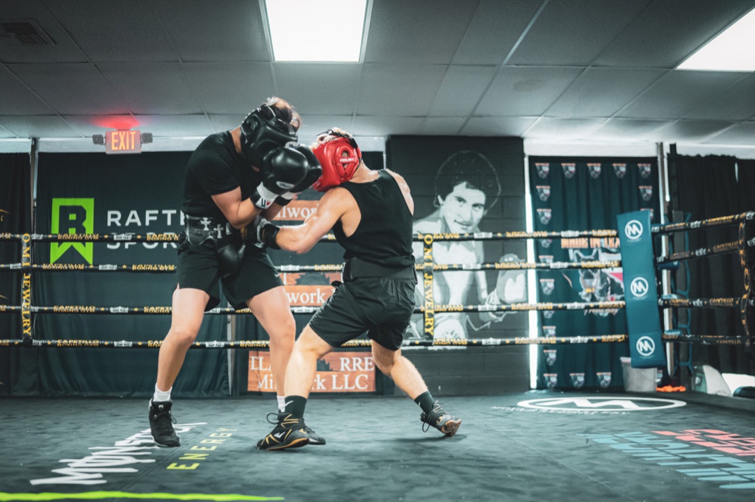 Two boxers spar in headgear inside a training ring.