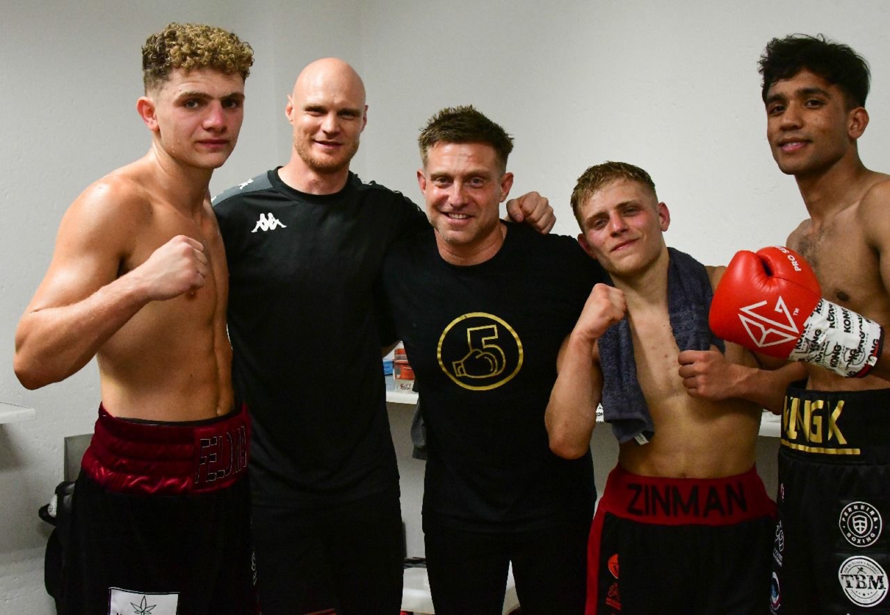 Five members of a fight team pose together in a changing room.