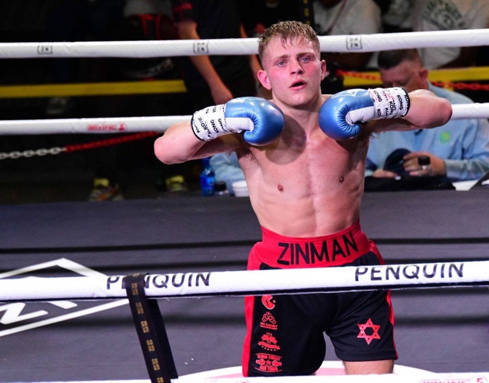 A boxer in blue gloves leans on the ropes between rounds.