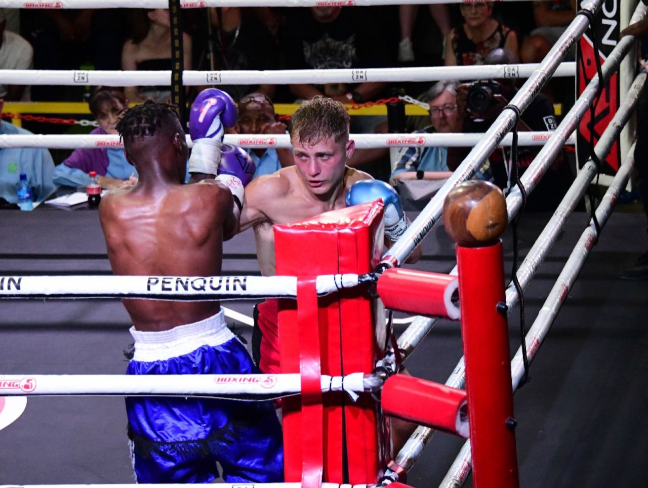 Two boxers exchange punches near the red corner.
